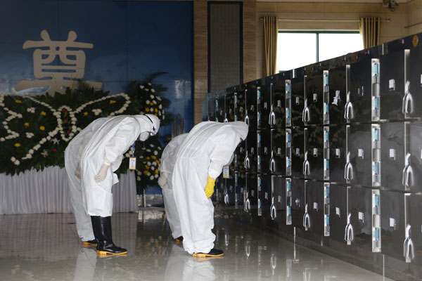 Morticians bow to containers holding the bodies of victims who died in the Eastern Star cruise accident at a funeral parlor in Jianli county, Hubei province, on Tuesday. (China Daily/Chen Zhuo)