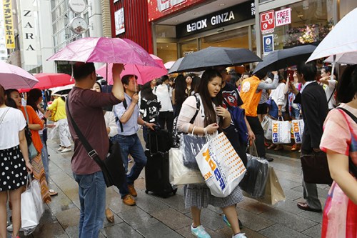 Chinese tourists with shopping bags wait for a sightseeing bus in front of a discount electronics store in Tokyo's Ginza district. The cheap yen, easier visas and other initiatives are luring foreign travelers eager to stretch their budgets, bringing in welcome cash. (Photo/China Daily)