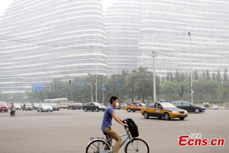 A cyclist wearing a face mask rides on a street on a smoggy day in Beijing, June 23, 2015.(Photo: China News Service/Li Huisi)