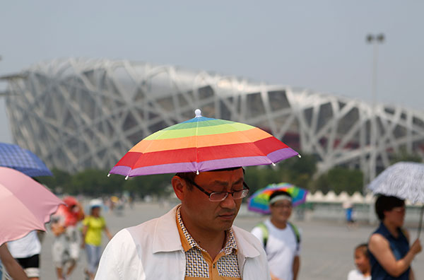 A tourist wears an umbrella hat to provide some shade while visiting the Beijing National Stadium on Sunday. WANG JING/CHINA DAILY
