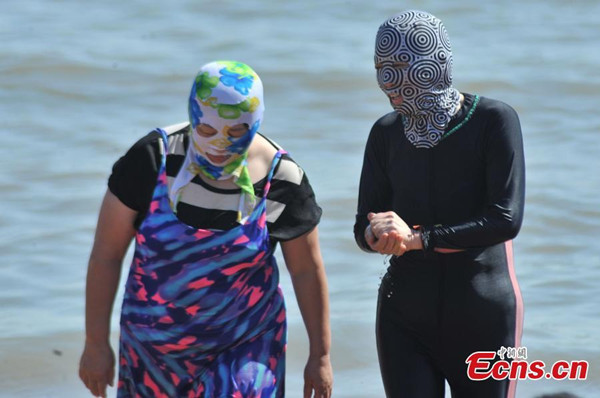 Swimmers wear facekinis on a beach in Qingdao city, East Chinas Shandong province, July 8, 2015.The mask is usually made out of wetsuit material and covers the wearers head, down to the collarbone with holes for the nose, eye and mouth. It became a fashion among beachgoers in Qingdao and other summer tourism destinations around China in recent years. (Photo/China News Service)