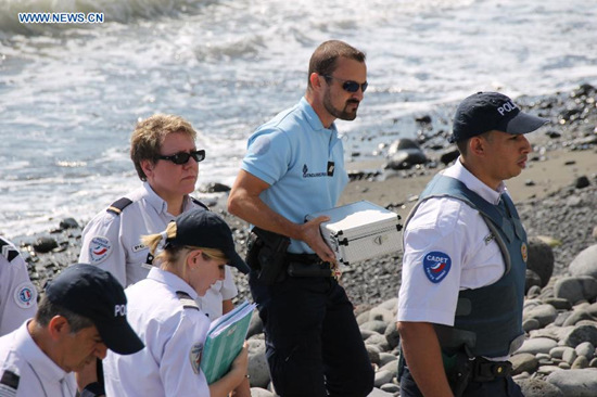Police officers leave the beach with a container holding metallic debris found on it in Saint-Denis, the Reunion Island, Aug. 2, 2015. (Photo: Xinhua/Romain Latournerie)
