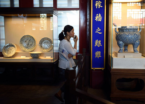 A visitor examines porcelains from the Ming Dynasty (1368-1644) during a three-month exhibition at the Palace Museum in Beijing in June. The porcelains on display are both perfect samples and restored ones from unearthed ceramic chips. (Jin Liangkuai/Xinhua)