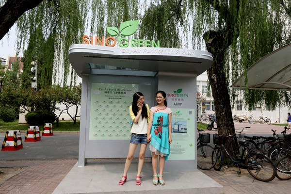 Two students wait for a school bus at a stop with an air purification device at Tsinghua University in Beijing in July. The apparatus was designed for outdoor air cleaning and has already been tested for four months at a bus stop in Hong Kong. CHINA DAILY