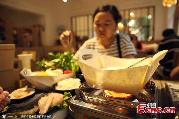 A diner enjoys the food briefly cooked and served in a paper hotpot at a restaurant in Shanghai municipality on August 28, 2015. As the citys first paper pot restaurants, the dining hall features facilities made from paper including tables, chairs and lamps. (Photo/CFP)
