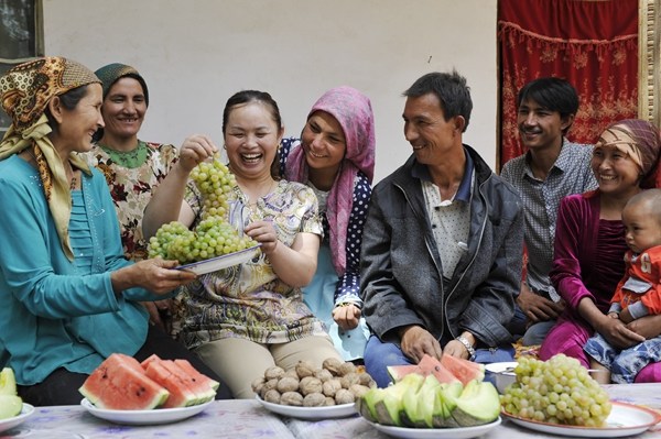You Liangying (second from left, front) visits Memeturop Musak (third from left, front) at his home in Pishan county, Hotan prefecture, on Sept 3.(YORTIK NIJAT/CHINA DAILY)