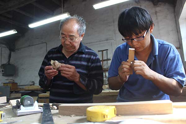 Huang Yongfang (left) checks components of a wooden model.(Photo by Wang Kaihao/China Daily)