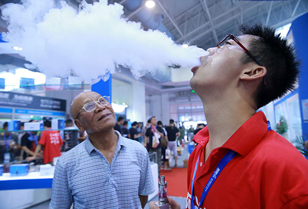 A visitor watches an assistant demonstrate cloud chasing at an e-cigarette exhibition in Beijing in July. (Photo: China Daily/Xiao Chen)
