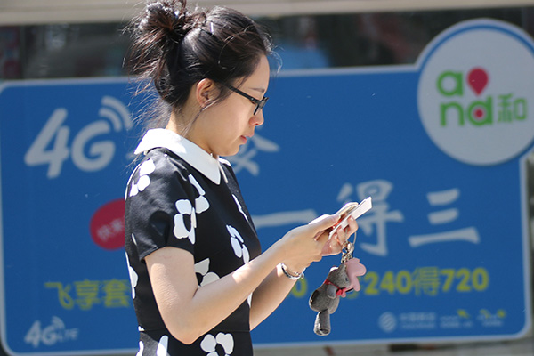 A mobile phone user walks past a logo of China Mobile's 4G service in Qingdao, Shandong province. (Photo/China Daily)