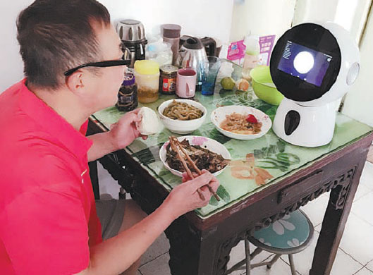 Chi Yunchang, a 60-year-old Shanghai resident, eats a meal while talking to Roby Mini, a robot tailor-made for the elderly market. Provided to China Daily