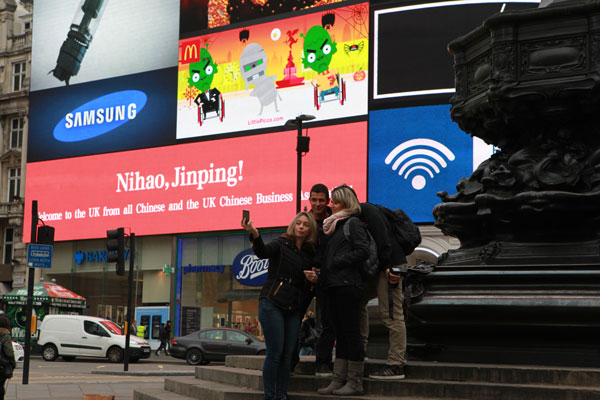 Visitors take picture at Piccadilly Circus, central London, where an electronic screen flashes Nihao, Jinping. (Tuo Yannan/China Daily)