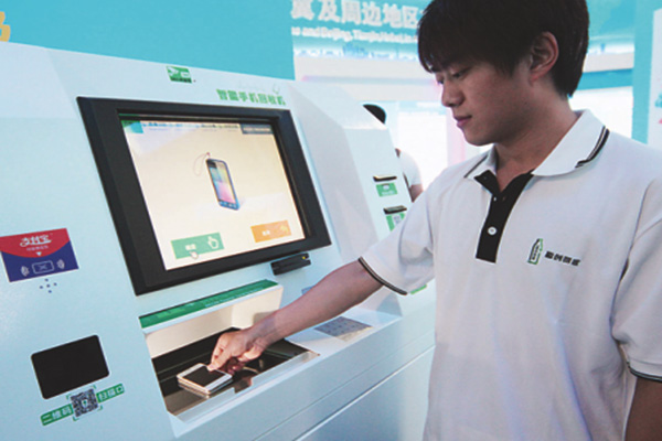 A man operates a machine that is capable of collecting used cellphones for recycling at a low-carbon technology fair in Beijing. (Photo/China Daily)
