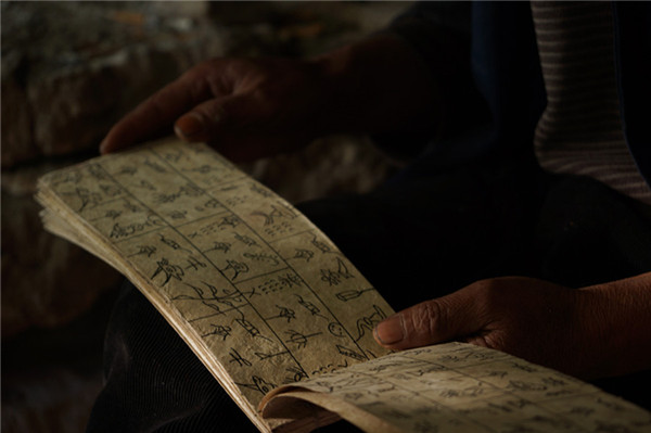 An aged villager reads Dongba scriptures written on traditional Dongba paper. (Photo by Xu Jing/chinadaily.com.cn)