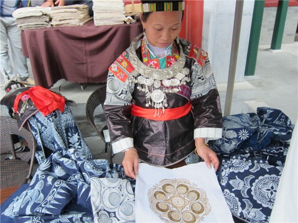Yang Chunyan from Guizhou sells batik pieces at a charity bazaar in Beijing. She also brings a wax-printed half-finished cloth for demonstration. (Photo by Sun Ye/China Daily)