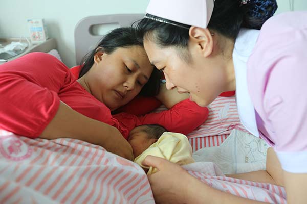 A nurse at a hospital in Xiangyang, Hubei province, helps Chen Jing to breast-feed her second child on Friday. GONG BO/CHINA DAILY