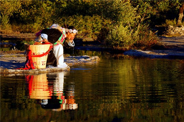 Worship is the obligation of a Dongba family. In early morning, Li Xiuhua goes to the Dongba altar on the hillside. She stops for a drink at a lake. (Photo by Xu Jing/chinadaily.com.cn) Worship is the obligation of a Dongba family. In early morning, Li Xiuhua goes to the Dongba altar on the hillside. She stops for a drink at a lake. (Photo by Xu Jing/chinadaily.com.cn)