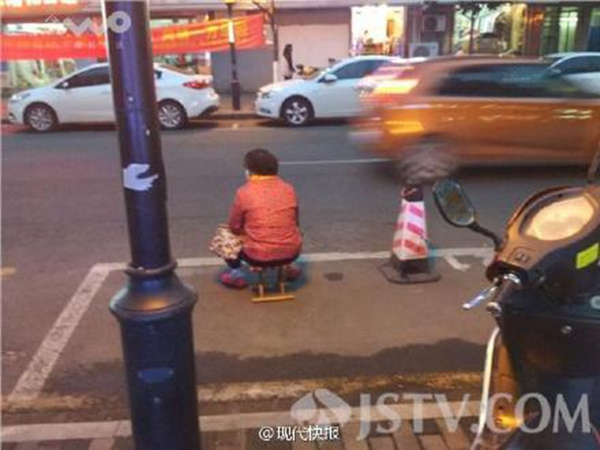 An elderly woman surnamed Zhou sits in a parking space to make sure nobody takes her son's parking space in Yancangqiao road, Nanjing of East China's Nanjing province. (Photo from Weibo)