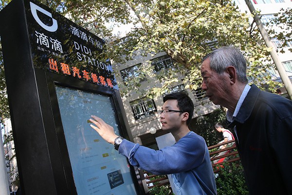 An employee of Didi Kuaidi shows a senior citizen how to book a car by using the touchscreen device at one of the many Didi stations installed by the company in Shanghai neighborhoods in October. (Photo/Xinhua)