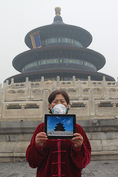Yang Shuqin, a 59-year-old tai chi practitioner in Beijing, holds an iPad at the Temple of Heaven on Tuesday as the city was shrouded in heavy smog. The iPad picture shows the landmark structure during good weather. ZOU HONG/CHINA DAILY