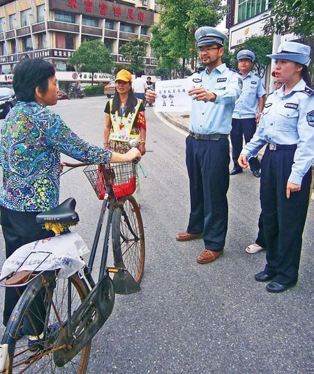 Josh Garcia, a temporary chengguan from the US, shows a pedestrian a sign saying "please do not jaywalk" in Zhuzhou, Hunan province. Governing the city in a civilized way is deemed a major goal of Chinese cities. (Photo/China Daily)