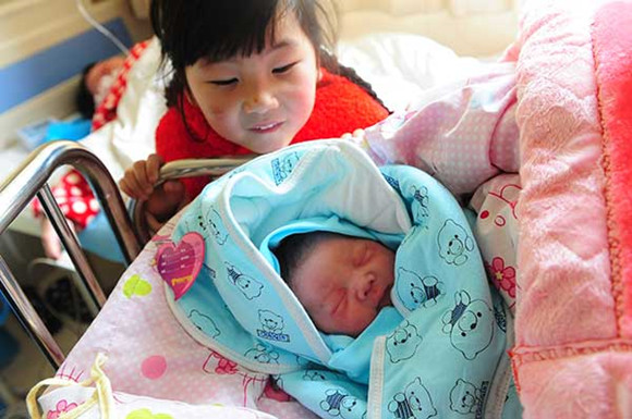 Xu Yuechen, a six-year-old girl, watches her newborn brother in a hospital in Fuyang, Anhui province, on Sunday.(Wang Biao/For China Daily)