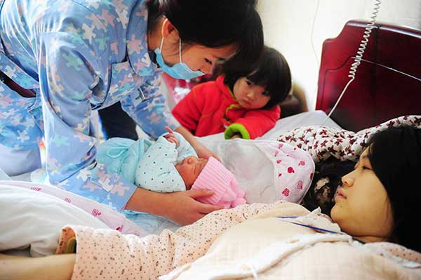 Six-year-old Xu Yuechen looks at her baby brother by the bed of her mother at a maternity hospital in Fuyang, Anhui province. (Photo: China Daily/Wang Biao)