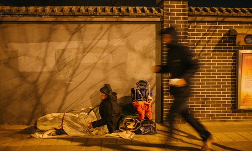 A man runs past a homeless person near Beijing South Railway Station on January 22, one of the coldest days this winter.(Photo: Global Times/Li Hao)