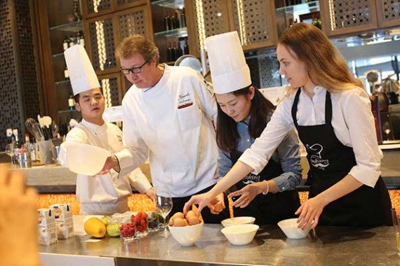 Pastry chef Cord H. Bredemeyer guides the cooking class to make Mille feuille of bitter and white couverture mousse on mangopapaya mirror at the Kempinskioperated Sunrise Hotel in Huairou district of Beijing. (Photo provided to China Daily)