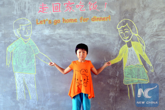 Liu Dongqing poses for photo with her parents painted on a blackboard in Nanguan Village of Chiping County, east China's Shandong Province, July 25, 2015. College students from the Academy of Fine Arts of Liaocheng University came to visit the left-behind children and empty-nest elderly persons, help them express their wish for family reunion with paintings. (Photo: Xinhua/Zhao Yuguo)