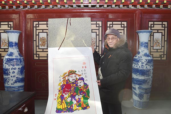 Guo shows one of the traditional New Year pictures. (Photo by Liu Xiangrui/China Daily)