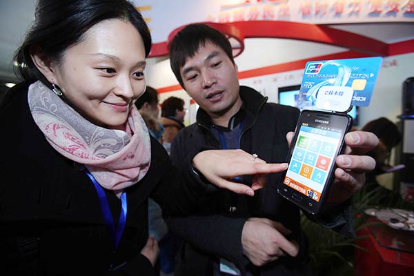 An employee shows a visitor how to use online payment functions on mobile devices at an expo in Beijing.(Photo/China Daily)