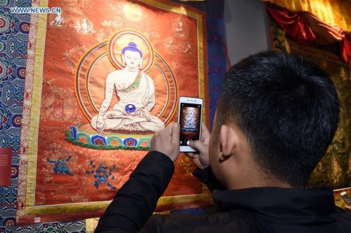 A visitor takes photos of a piece of Thangka work at an exhibition of Tibetan Thangka painting in Lanzhou, capital of northwest China's Gansu Province, Jan. 18, 2016. Thangka, a Tibetan scroll-banner depicting various kinds of contents, has become a valuable kind of collection in recent years. (Photo: Xinhua/Fan Peishen)