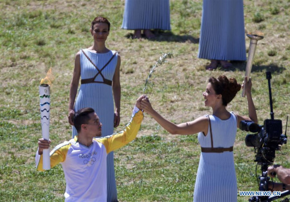 Katerina Lechou (R) acting the high priestess hands an olive branch to Eleftherios Petrounias, Greece's artistic gymnast, during the Olympic flame lighting ceremony for the Rio 2016 Olympic Games inside the ancient Olympic Stadium on the site of ancient Olympia, Greece, April 21, 2016. (Photo: Xinhua/Jin Yu)