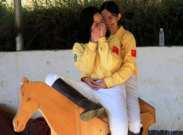 Mo Lianyu and Lu Cuiting sit on a wooden horse, which is used for students to practice horse riding. HUO YAN/REN QI/CHINA DAILY