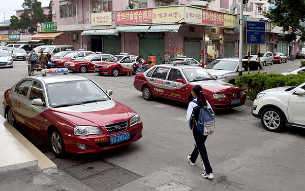 A woman walks along a street lined with taxis in Dawang village, Shenzhen, Guangdong province, in February. The village is home to many taxi drivers and their families. Zhang Wei/For China Daily