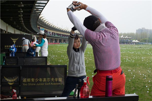 A boy practices under the guidance of a coach at the Yao Shine Golf School in Shanghai on April 9.GAO ERQIANG/CHINA DAILY