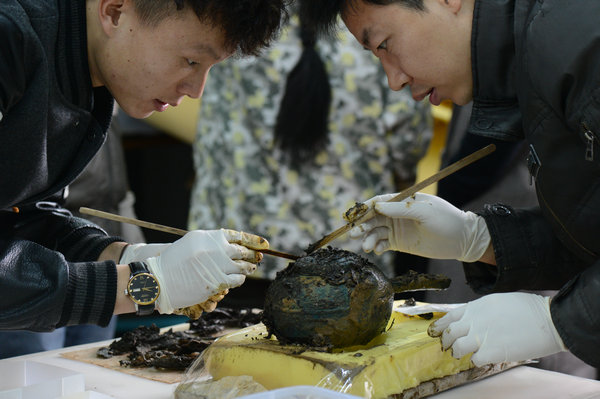 Two archaeologists clean a bronze vessel unearthed from the excavation of the Marquis Haihun's tomb in Nanchang, Jiangxi province (Photo provided to China Daily)
