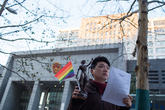 Xiao Zhen stands holding the judgment that rules against a psychological counseling center offering gay conversion therapy in Beijing. Photo: Courtesy of Xiao Zhen