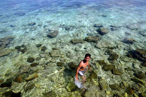 A man stands in shallow water near Yongxing Island, which was once home to coral reefs. (Photo provided to China Daily)