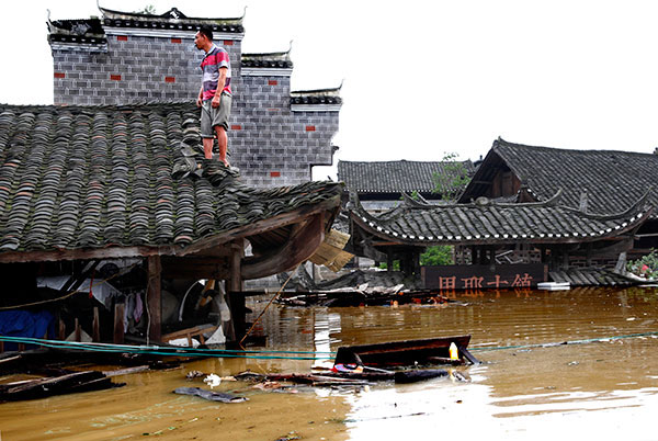 A man stands on the roof of his home, which is steeped in water in the ancient town of Liye in Longshan county, Hunan province, on Tuesday. (Photo/China Daily)