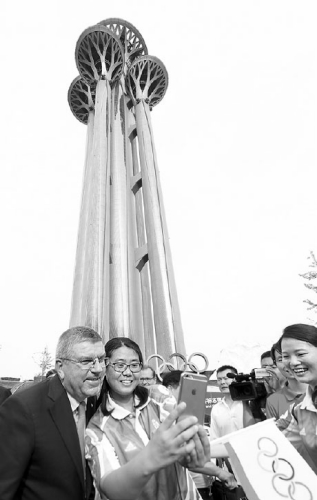 Thomas Bach, president of the International Olympic Committee, stands for photos with volunteers near the newly named Beijing Olympic Tower on Sunday. Zou Hong / China Daily