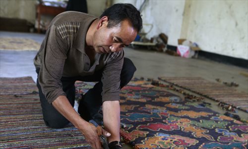 A man cuts off the extra hanging threads from a newly-woven carpet. Photo: Li Hao/GT