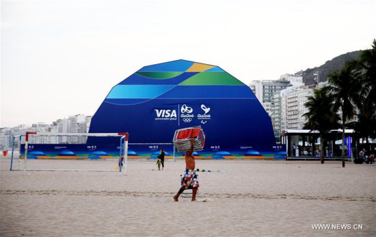 Photo taken on July 8, 2016 shows a man carring beach chairs passing the megastore at the Copacabana beach, in Rio de Janeiro, Brazil. The 2016 Rio Olympic Games will be held from August 5 to 21. (Photo/Xinhua)