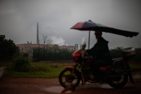 A motorbike passes a chemical factory that discharges smoke in Hengdong.(YANG YI/CHINA DAILY)