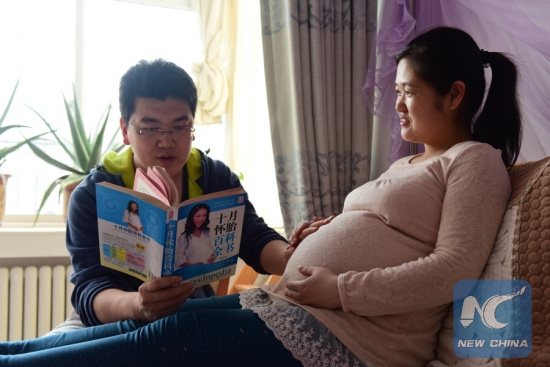 Nurse Song Mingming (L) reads a book to his wife Yu Junxia, who is pregnant, at home in Yantai, east China's Shandong Province, May 10, 2016. (Xinhua/File Photo)