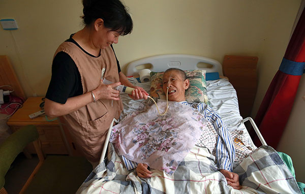 A caregiver helps feed Wang Lingfang, a bedridden 68-year-old patient, via a feeding tube at Puleyuan Nursing Home in Beijing.(Zou Hong/China Daily)