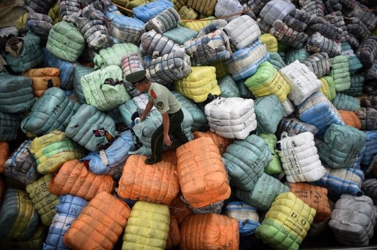 A frontier police officer from Shenzhen in Guangdong Province walks on a hill piled up with smuggled used clothes on August 9. (Photo/Xinhua)