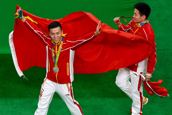 Silver medallist Dong Dong of China (left) and bronze medallist Gao Lei of China pose with their national flags after the men's trampoline final in Rio de Janeiro, Brazil, August 13, 2016. (Photo by Wei Xiaohao/chinadaily.com.cn)