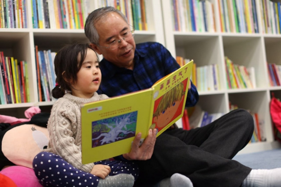 A grandfather reads stories to his granddaughter at a library in Beijing. The middle class read more than the national average by a large margin. (Photo: China Daily/Asianewsphoto]