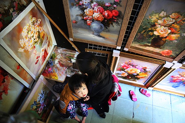 An oil painter works on a still life painting as her daughter sits on her lap at an art gallery in Dafen village, Shenzhen, Guangdong province. (Photo by Xu Yuanchang/China Daily)